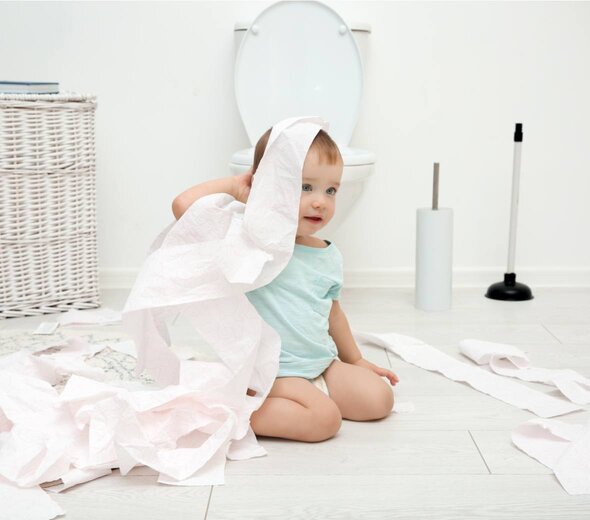 Dziecko bawi się papierem toaletowym. W okół niego jest mnóstwo rozrzuconego po całej łazience papieru, co sprawia mu radość.