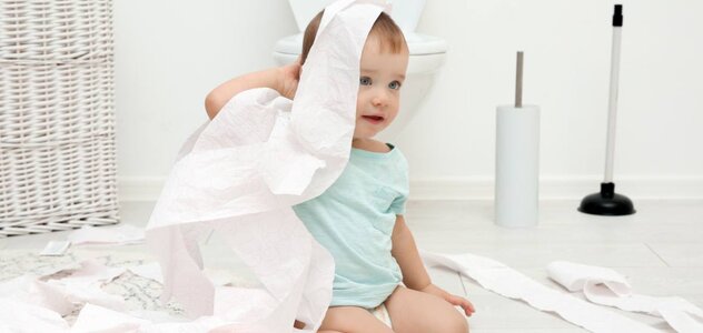 Dziecko bawi się papierem toaletowym. W okół niego jest mnóstwo rozrzuconego po całej łazience papieru, co sprawia mu radość.