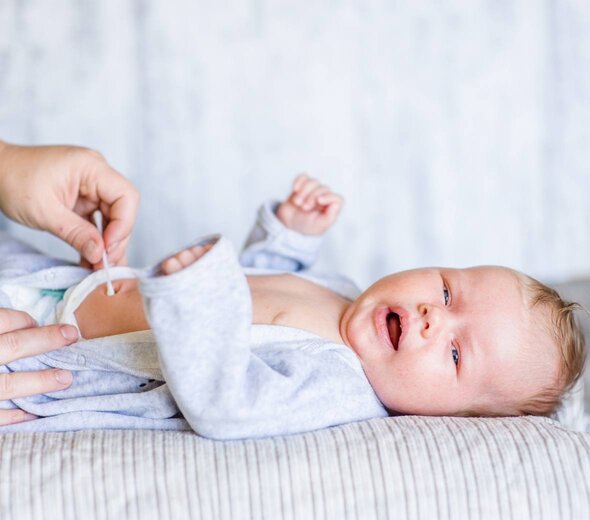 Dziecko leży na plecach, podczas gdy rodzic przemywa jego kikut pępowinowy patyczkiem. 