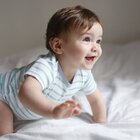  The baby is crawling on the bed. He has a white body with green stripes. He is laughing. He has brown hair.