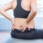 A woman in advanced pregnancy, just before giving birth, performs loosening exercises to facilitate preparation for childbirth. Expectant mother dressed in sports outfit sits on a large ball and props with her hands in the lumbar spine.