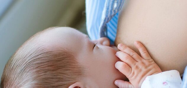 A small baby is put to the breast and is happy to drink mother's natural, nutritious milk. The baby is lying with a nipple in its mouth and his hand is holding the breast from which he is sucking milk.