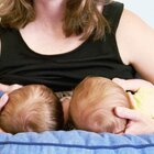 The mother visible in the picture supports two heads of twins with her hands. The babies are laid on their knees and facing the woman who puts them on her breast and feeds her mother's milk.
