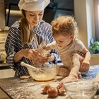 A young mother spends time with her several-month-old baby in the kitchen. A woman is making cookies with the baby. The infant is sitting on the counter alone and is helping mom in cooking.