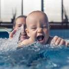  The newly mother stays together with the child of several months in the pool. The baby has a great time splashing in the water. The mother belays the baby and keeps it on the surface.