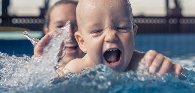  The newly mother stays together with the child of several months in the pool. The baby has a great time splashing in the water. The mother belays the baby and keeps it on the surface.