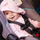 A recently born baby with a wide smile ia sitting calmly in a baby car seat. Baby is wearing in a pink sweatshirt with tiny ears sewn on the hood.