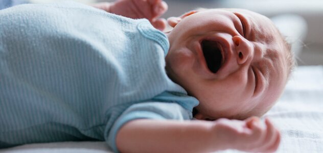 The newborn baby is lying on the bed on his back. The child lifting his arms up and moving his hands in anger. The infant opens its mouth wide and closes its eyes tightly when is crying.