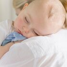 The young mother stays with her newborn baby at home. The woman is hugging her newborn baby. The child cuddles the head into the shoulder of the parent and hugging the blue blanket, sleeping well.