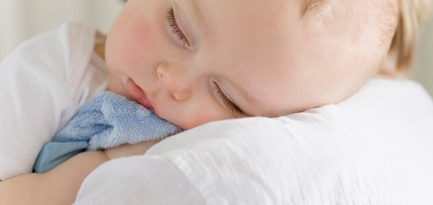 The young mother stays with her newborn baby at home. The woman is hugging her newborn baby. The child cuddles the head into the shoulder of the parent and hugging the blue blanket, sleeping well.