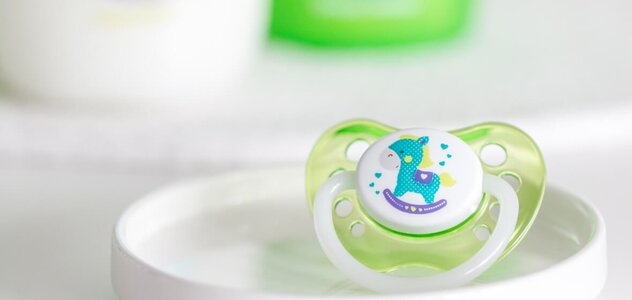 On a white, small plate on the dresser lying a green soother with a rocking horse motif. The selection of a suitable teat is very important for the development of the speech apparatus.