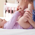A young mother spends time with her newborn baby. The newborn baby is lying on his back on the changing table. The parent holds the baby feet in her hands and kisses one of the feet.