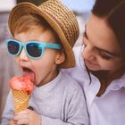   Poznaj wymowę A young mother enjoys spending time with her little son. The boy wearing blue glasses, a straw hat and a sweatshirt, he is sitting on his parent's knees and eats strawberry ice cream.
